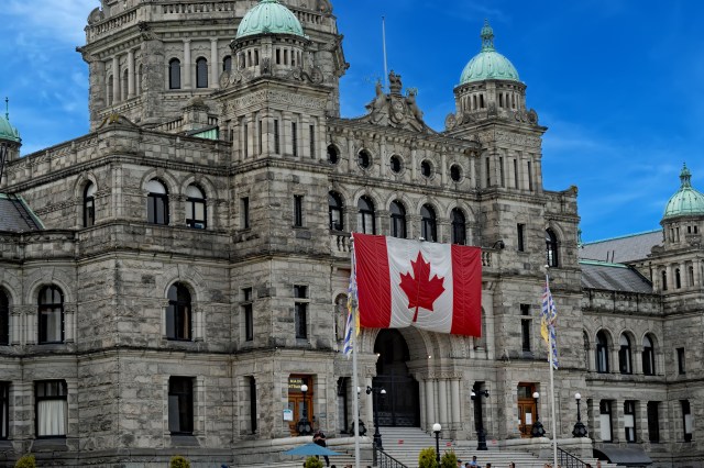 The British Columbia Parliament Buildings in Victoria, Canada, featuring a large Canadian flag hanging prominently from the front.