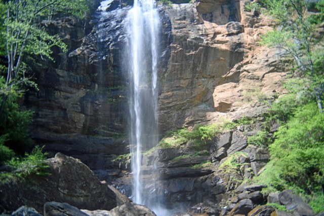 A scenic waterfall cascading down a rocky cliff, surrounded by greenery and trees.